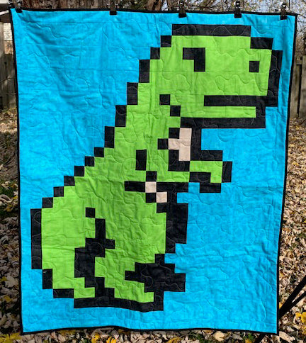 Finished T-Rex pixel quilt in green on bright blue, machine quilted, photographed hanging outdoors